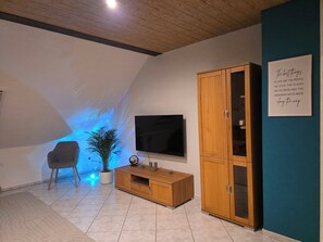 A modern living room with a flat-screen TV, wooden cabinet, and a potted plant.