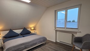 Ein Schlafzimmer mit einem Bett, Nachttischlampen, einem Sessel, einem Fenster und einer Heizung.