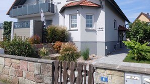 Ein zweistöckiges Haus mit Balkon und einer Steinmauer davor, mit der Hausnummer 8.