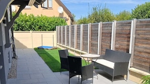 Ein Außenbereich mit einer Terrasse, einer Sitzgruppe, einem gepflasterten Weg und einem Holzzaun.