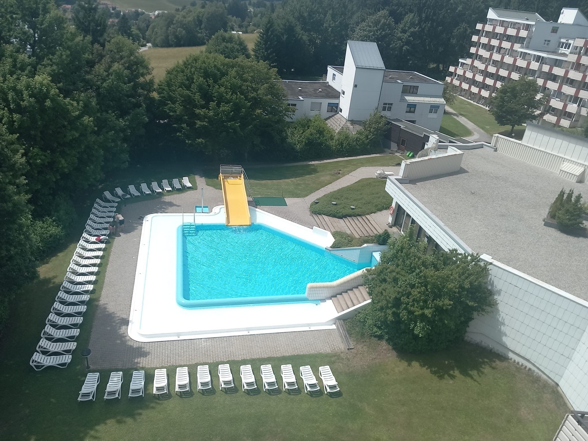 Una piscina con tobogán, rodeada de sillones de descanso y un edificio de techo plano.