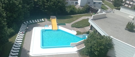 Una piscina con tobogán, rodeada de sillones de descanso y un edificio de techo plano.