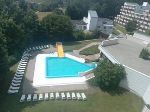 Ein Schwimmbecken mit Rutsche, umgeben von Liegestühlen und einem Gebäude mit flachem Dach.
