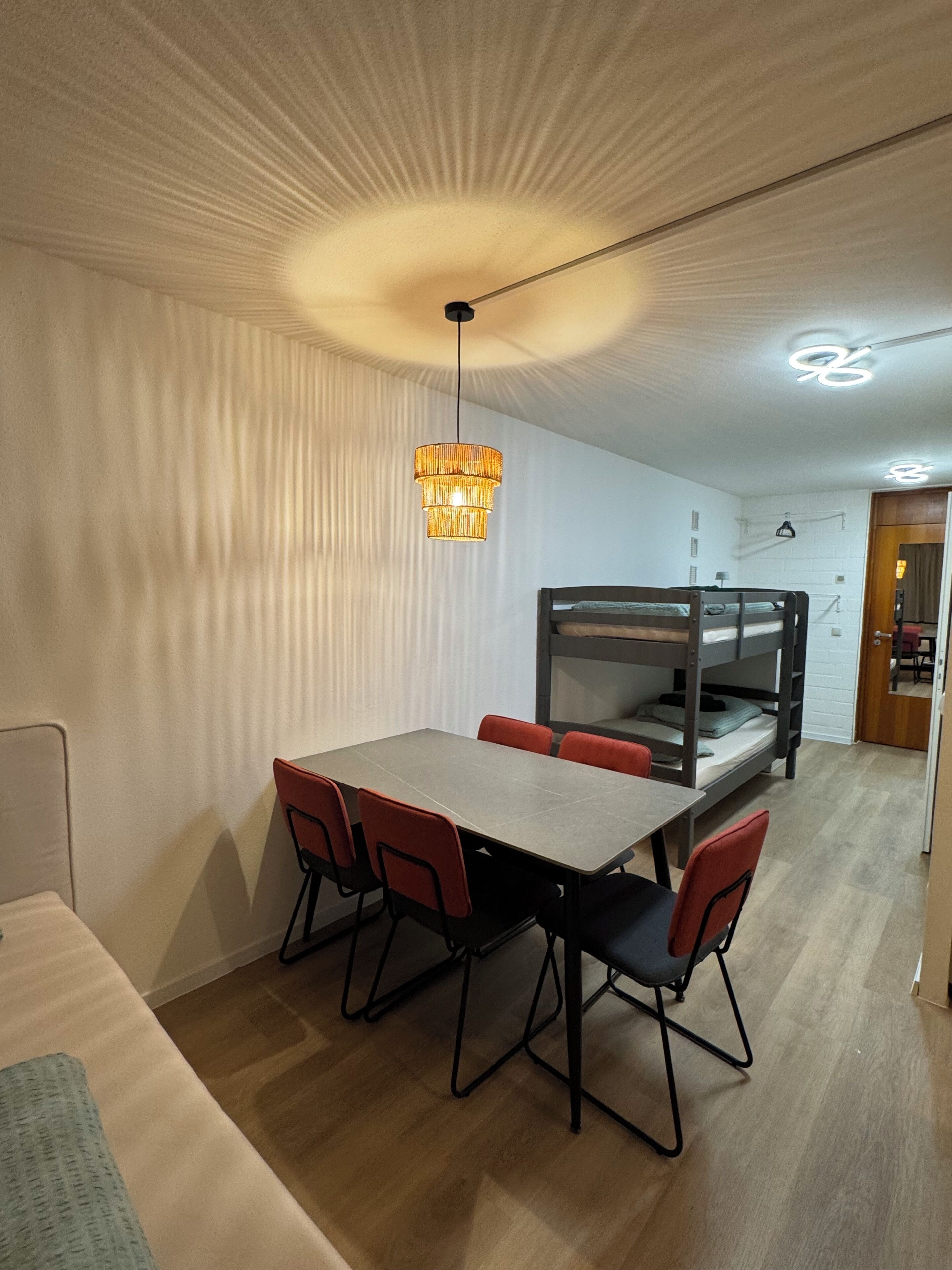 Une pièce avec un lit superposé, une table à manger avec des chaises et un luminaire suspendu.