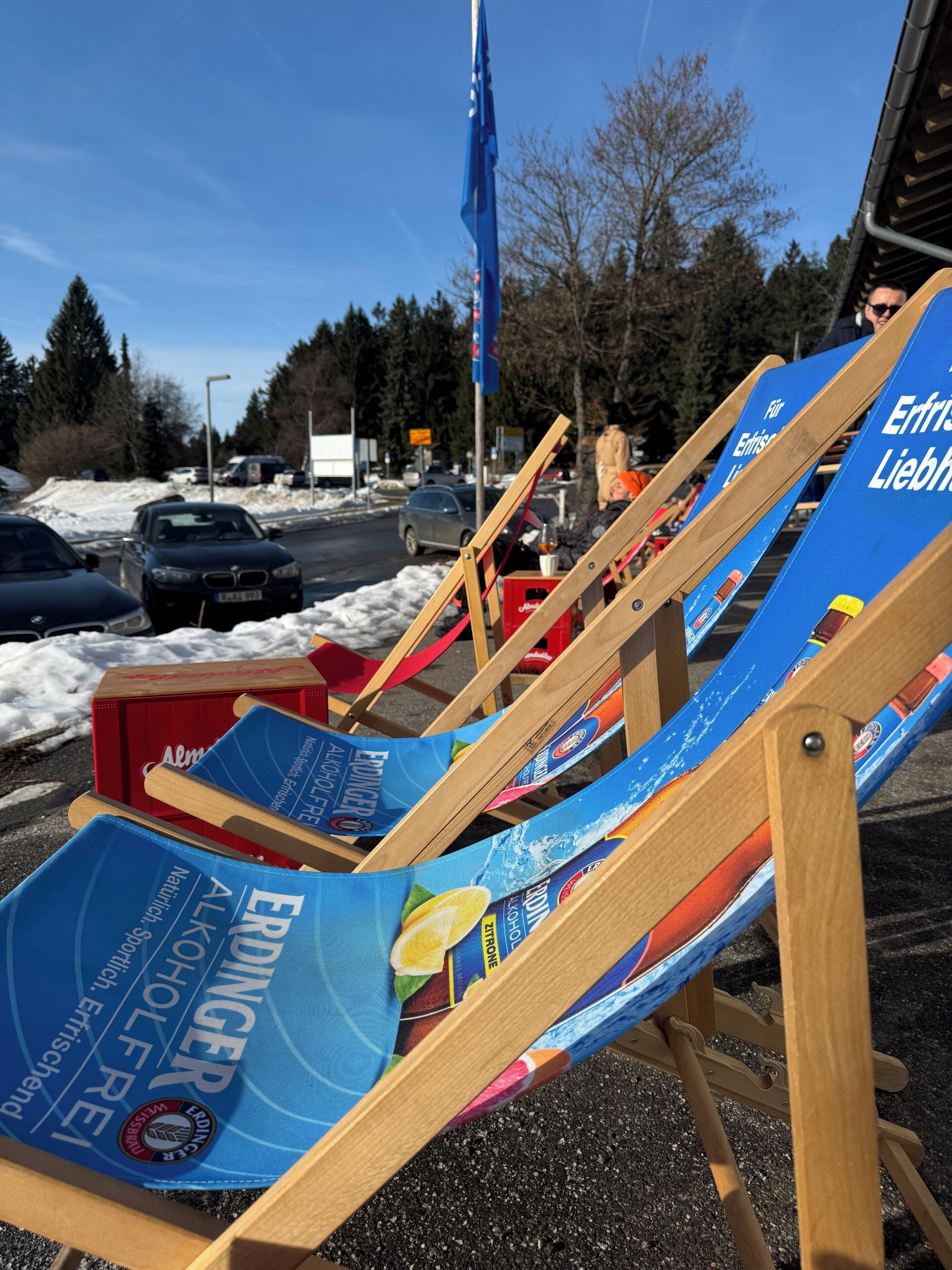 Outdoor wooden lounge chairs with blue cushions advertising alcohol brands, parked on a gravel surface.