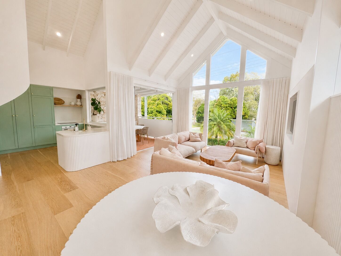 A spacious living area with a large window, a kitchen with green cabinets, and a round coffee table.