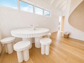 Un intérieur moderne avec une table ronde et des tabourets assortis, un mur blanc à texture et un plancher en bois.