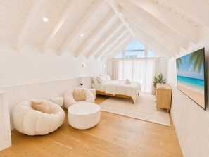 Une chambre moderne avec un plafond de style industriel, un lit, un coin salon avec un pouf rond et une grande fenêtre avec des rideaux.