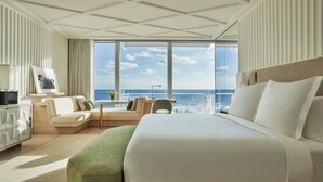 A hotel room with a large bed, a seating area with a view of the sea, and a desk with a chair. - Four Seasons Hotel at The Surf Club.  (Surfside)