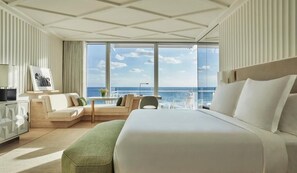 Habitació d'hotel amb un llit gran, zona de seients amb vista al mar i escriptori amb cadira.