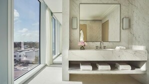 A modern bathroom with a large mirror, marble countertop, and a view of the city through a large window. - Four Seasons Hotel at The Surf Club.  (Surfside)