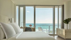 A hotel room with a large bed, a desk, a chair, and a view of the ocean. - Four Seasons Hotel at The Surf Club.  (Surfside)