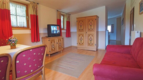 A living room with a television, a red sofa, a wooden cabinet, and a dining area with a table and chairs. - Vrbo Property (Berchtesgaden)