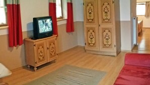 A room with a wooden cabinet, a television on a stand, a red sofa, and a patterned rug. - Vrbo Property (Berchtesgaden)
