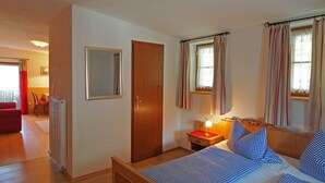 A bedroom with a bed, a bedside table with a lamp, a wooden door, and a window with curtains. - Vrbo Property (Berchtesgaden)