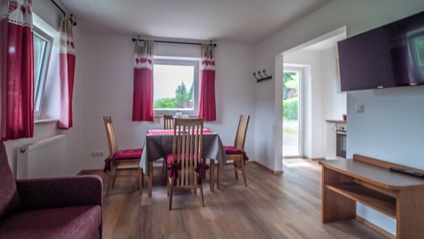 A room with a dining table, chairs, a sofa, a TV, and a window with curtains. - Vrbo Property (Berchtesgaden)