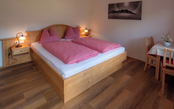 A wooden bed with checkered bedding, bedside lamps, a small table with a vase, and a chair. - Vrbo Property (Berchtesgaden)
