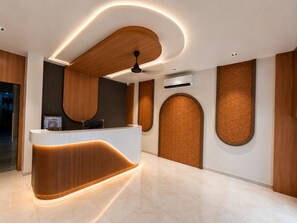 A modern reception area with a curved reception desk, wooden paneling, and a ceiling fan. - Hotel Teerth Dwarka (Dwarka)