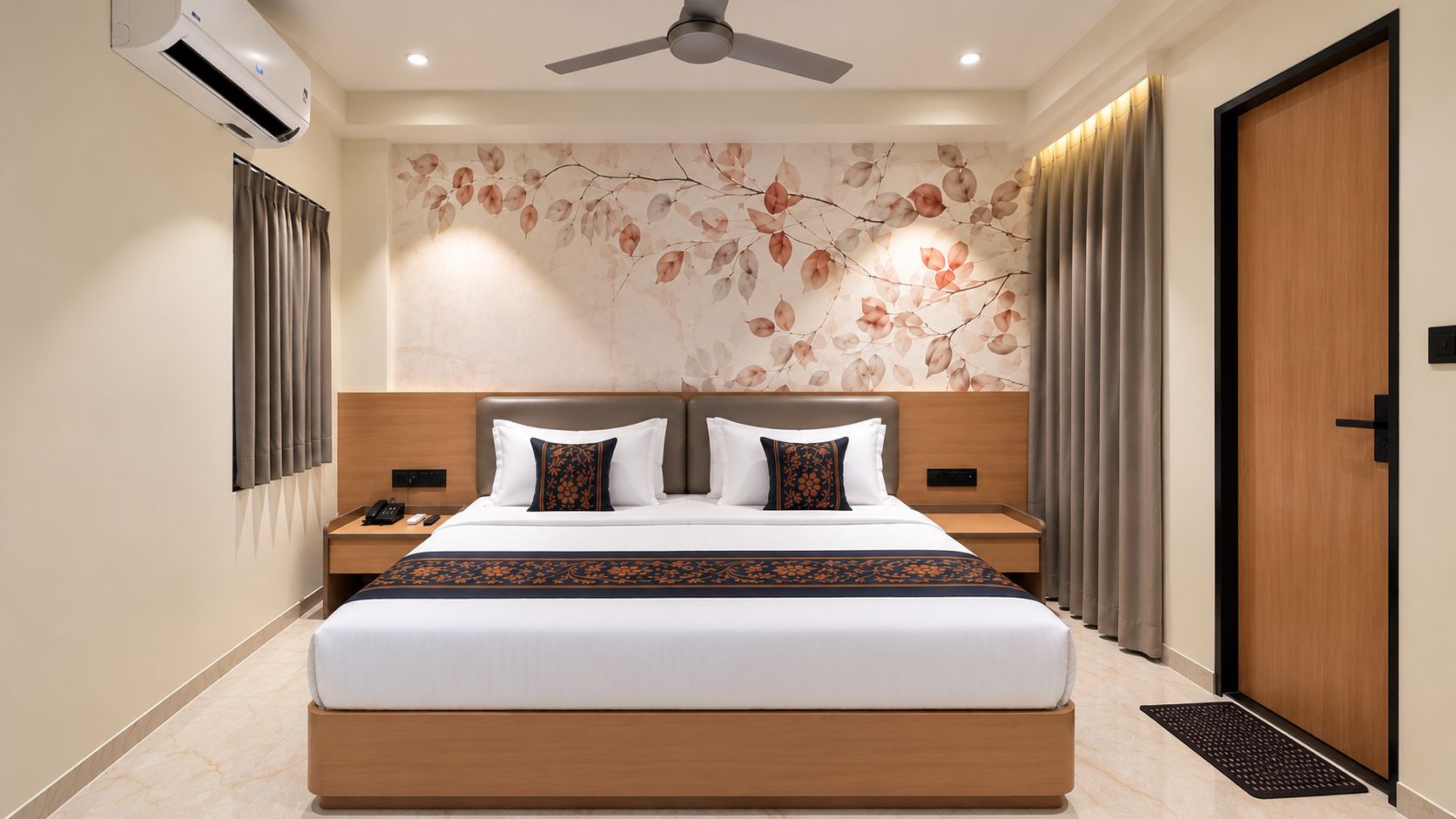 Une chambre d’hôtel avec un grand lit, un ventilateur de plafond, un climatiseur fixé au mur et une porte avec un cadre en bois.