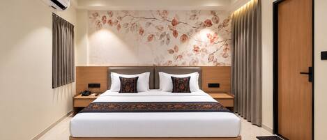Une chambre d’hôtel avec un grand lit, un ventilateur de plafond, un climatiseur fixé au mur et une porte avec un cadre en bois.