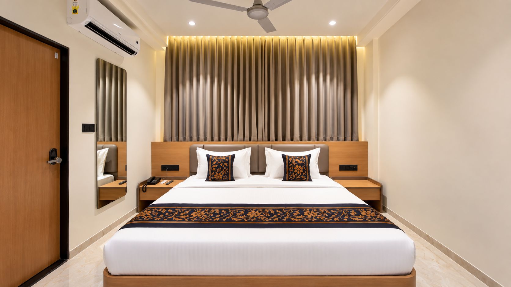 Une chambre d’hôtel avec un grand lit, une table de chevet avec un téléphone, une commode, un miroir et un ventilateur de plafond.