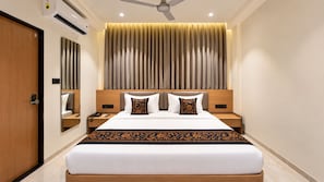 A hotel room with a large bed, a bedside table with a phone, a nightstand, a mirror, and a ceiling fan. - Hotel Teerth Dwarka (Dwarka)