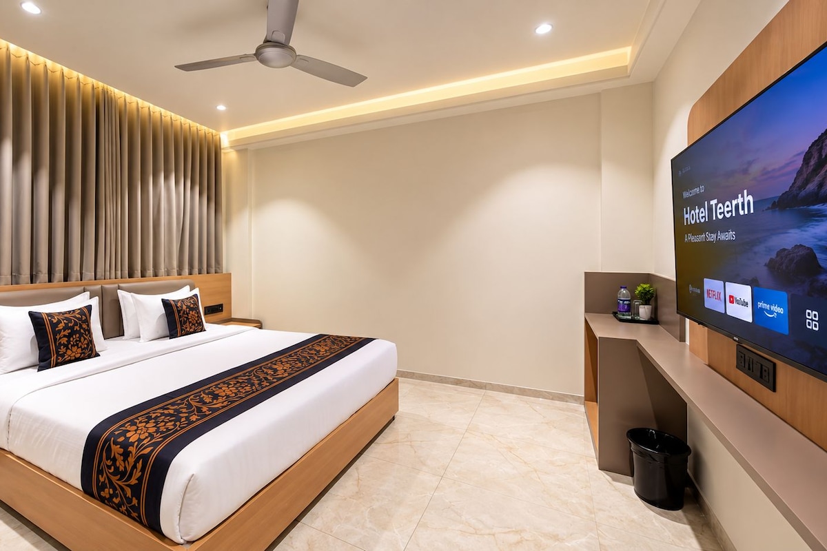 Una habitación de hotel con una cama, televisor y un escritorio con computadora y teléfono.