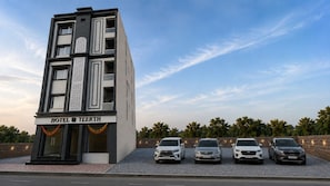 Un edificio de hotel de varios pisos con un letrero que dice 'HOTEL TEERTH'. Hay cuatro coches estacionados al frente.