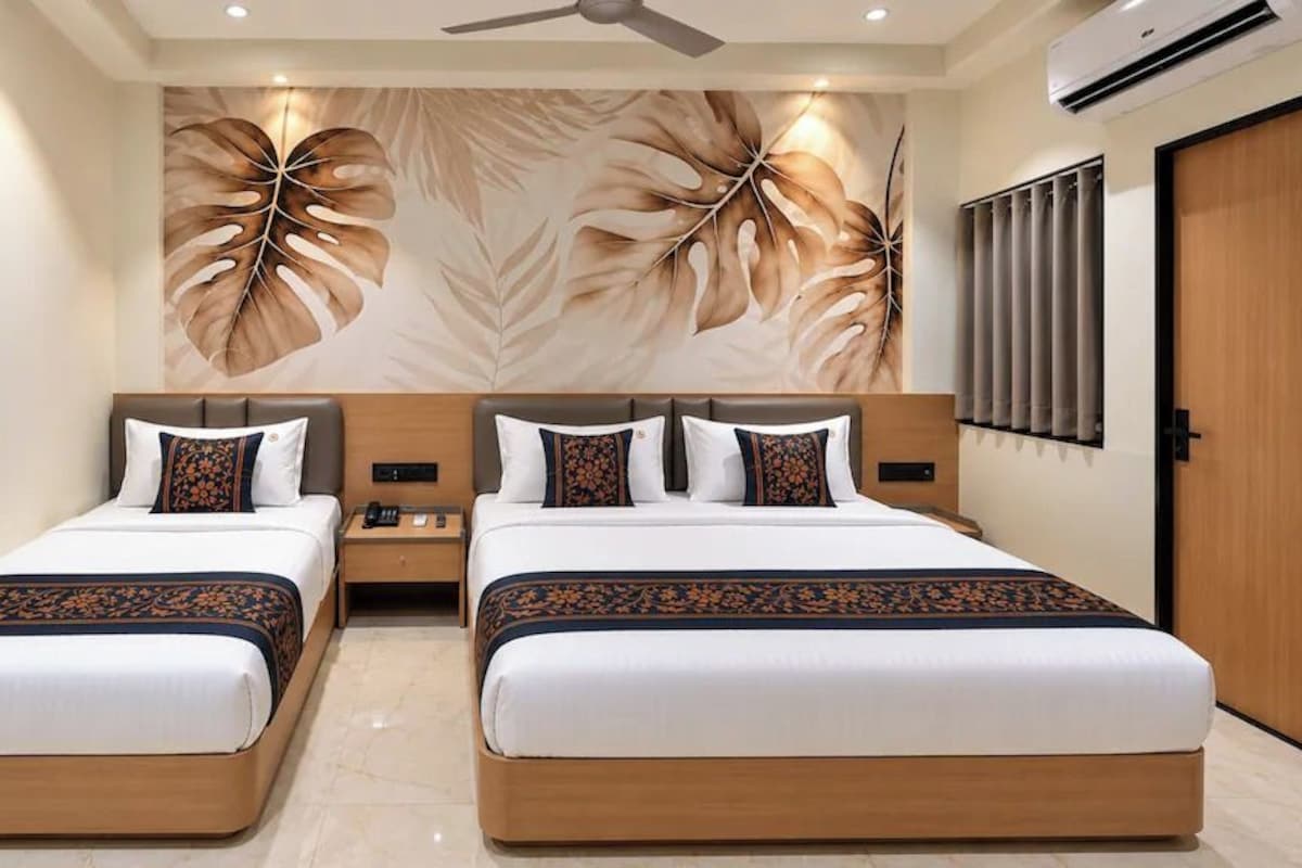 A hotel room with two beds, a ceiling fan, an air conditioning unit, and a wall with a leaf pattern.