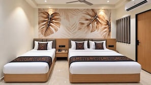 A hotel room with two beds, a ceiling fan, an air conditioning unit, and a wall with a leaf pattern. - Hotel Teerth Dwarka (Dwarka)