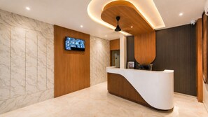 Una zona de recepción con piso de mármol, mostrador de madera, televisor montado y ventilador de techo.