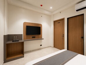 A hotel room with a bed, a mounted TV, a wardrobe, and a shelf with bottles. - Hotel Teerth Dwarka (Dwarka)