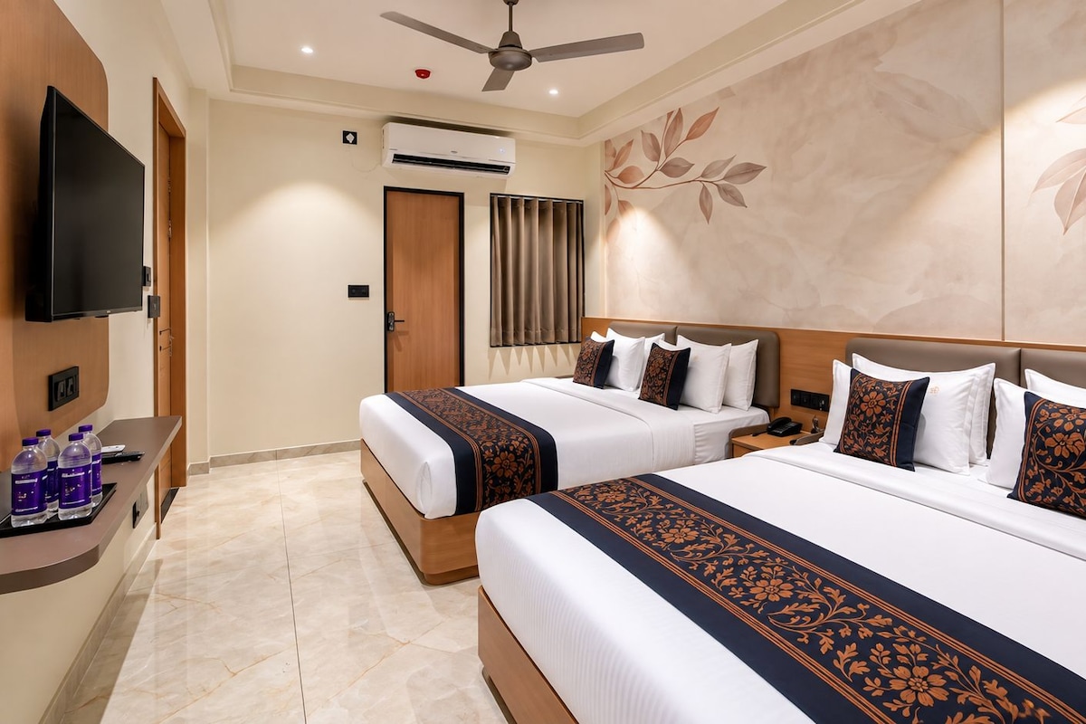Habitación de hotel con dos camas, televisión, aire acondicionado y un mostrador de recepción con botellas de agua.