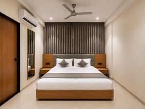 A modern hotel room with a large bed, two bedside tables, a ceiling fan, and a large window with curtains. - Hotel Teerth Dwarka (Dwarka)