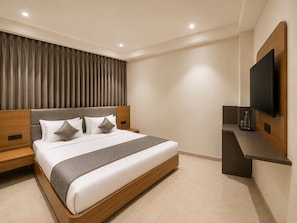 A modern hotel room with a large bed, a flat-screen TV mounted on the wall, and a built-in bench at the foot of the bed. - Hotel Teerth Dwarka (Dwarka)