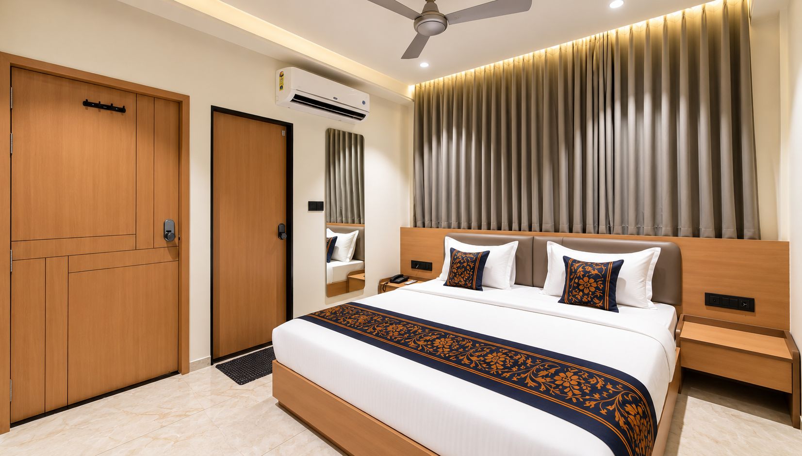 Una habitación de hotel con cama, mesitas de noche, un equipo de aire acondicionado, un ventilador de techo y un amplio ventanal con cortinas.
