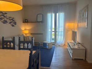 A room with a sofa, a small table, a TV, and a window with curtains. - Casa Indaco – Lake View, terrace & relax (Padenghe sul Garda)