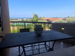 A balcony with a table and chairs, overlooking a pool and distant buildings. - Casa Indaco – Lake View, terrace & relax (Padenghe sul Garda)