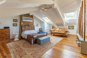 Ein Schlafzimmer mit schrägem Dach, Holzboden, einem Bett, einem Schrank, einem Stuhl und einem Dachfenster.