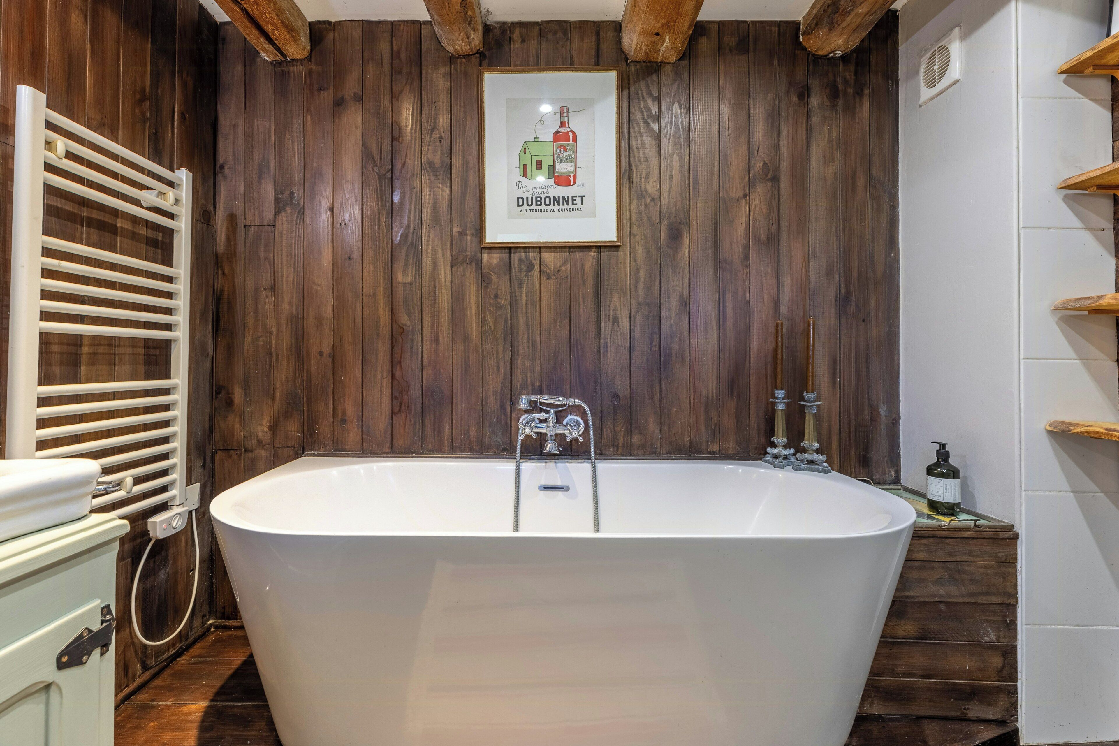 Ein Badezimmer mit freitstehender Badewanne, Holzvertäfelung, einem Heizkörper und einem gerahmten Poster an der Wand.