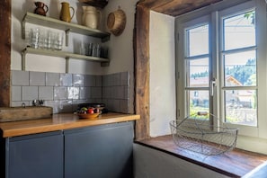 A kitchen with a wooden countertop, a sink, and a window with a view of a house and trees. - Stone house in the hills of the Livradois (Marsac-en-Livradois)