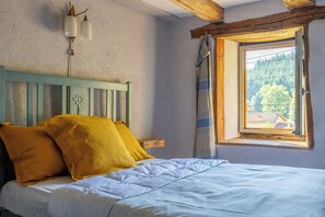Ein Schlafzimmer mit einem Bett, einem hölzernen Kopfstück, einem Fenster mit Vorhängen und Blick auf Bäume und Gebäude.