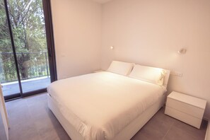 A bedroom with a large bed, a nightstand, and a window with a view of trees. - Residence Domus 1 Treviso Family Suites (Treviso)