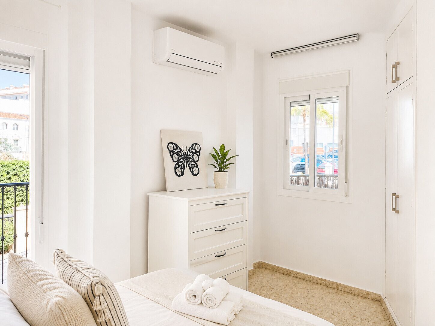 Une chambre d’hôtel avec un lit, une table de chevet agrémentée d’une plante, une fenêtre donnant sur un paysage agréable et un appareil de climatisation.