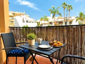 A balcony with a table set for breakfast, including croissants, a potted plant, and a cup. - Apartment La Cala Blanc in Cala Del Moral (Rincón de la Victoria)
