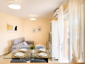 A modern living room with a glass dining table set for four, a grey sofa, and a white air conditioning unit. - Apartment La Cala Blanc in Cala Del Moral (Rincón de la Victoria)