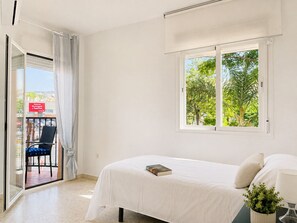 A bedroom with a bed, a window with a view of trees, a chair, and a balcony with a view of the street. - Apartment La Cala Blanc in Cala Del Moral (Rincón de la Victoria)