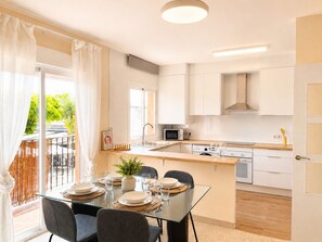 A modern kitchen with a glass dining table, white cabinets, and a view of greenery outside. - Apartment La Cala Blanc in Cala Del Moral (Rincón de la Victoria)