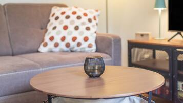 A round wooden table with a decorative vase in the center, a sofa with a polka dot pillow, and a lamp on a side table.