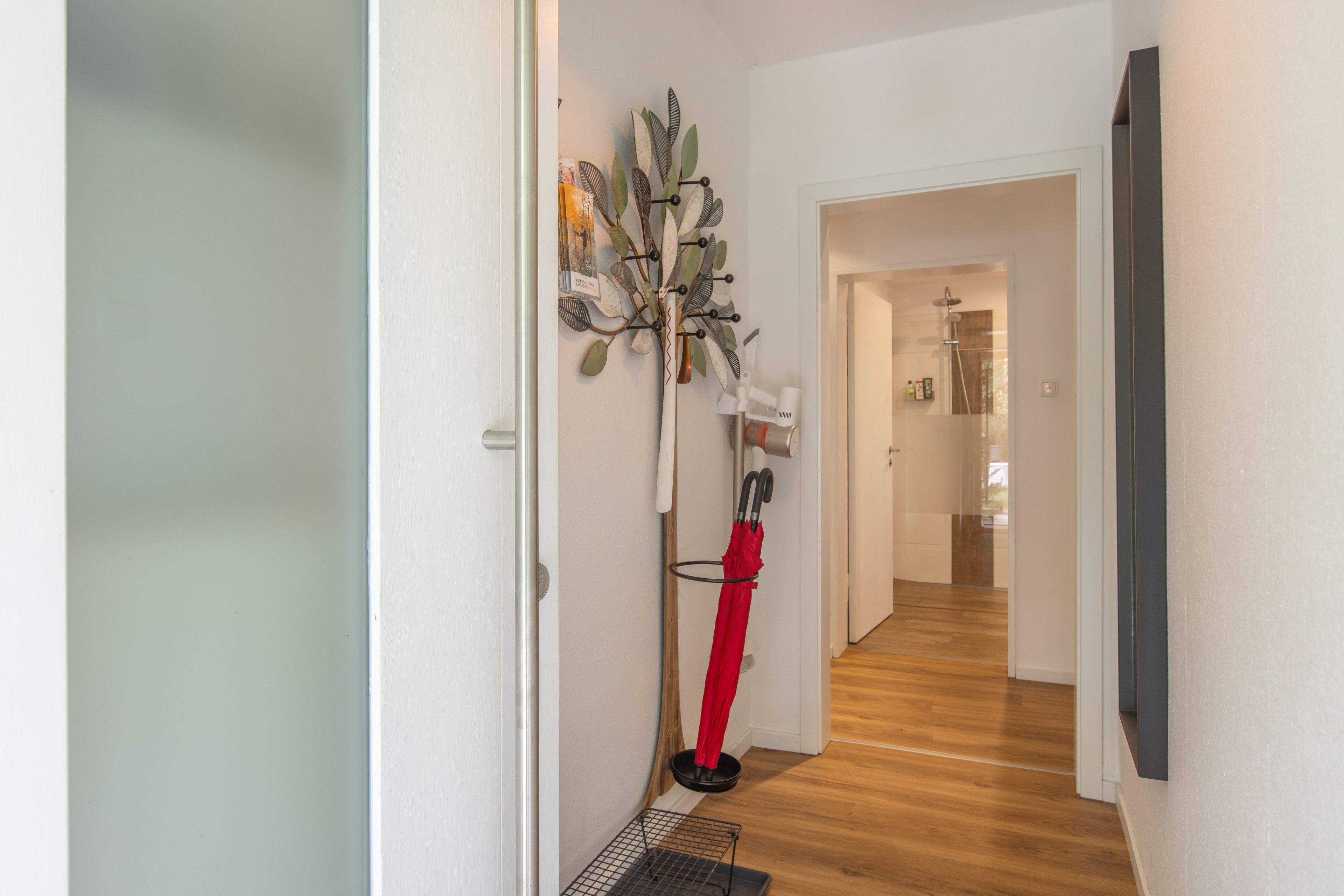 Un couloir doté d’un plancher en bois, un porte-manteau sur lequel sont accrochés divers objets, et une porte donnant sur une autre pièce.